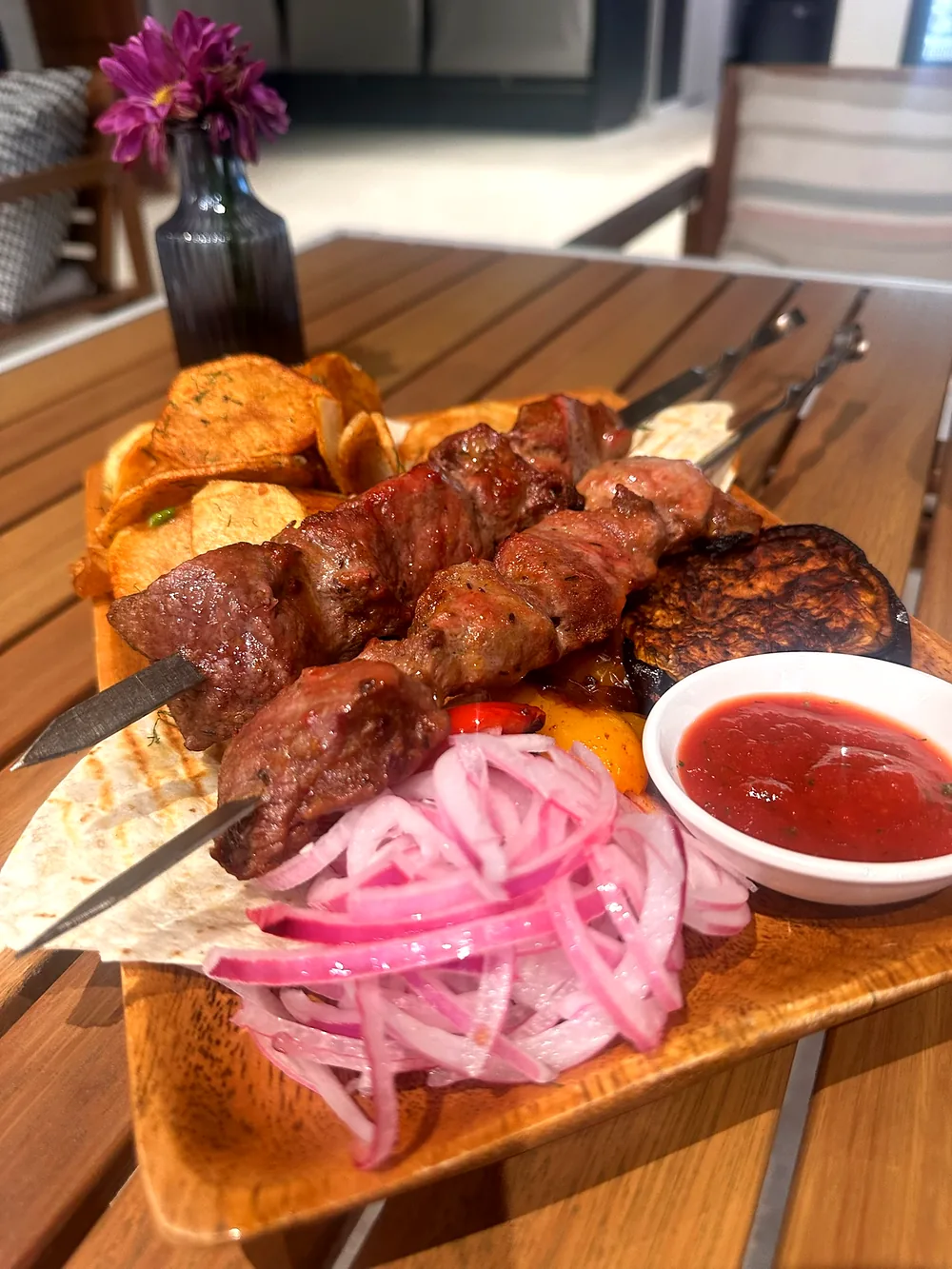 A wooden board of grilled meat with pickled onions and sauce