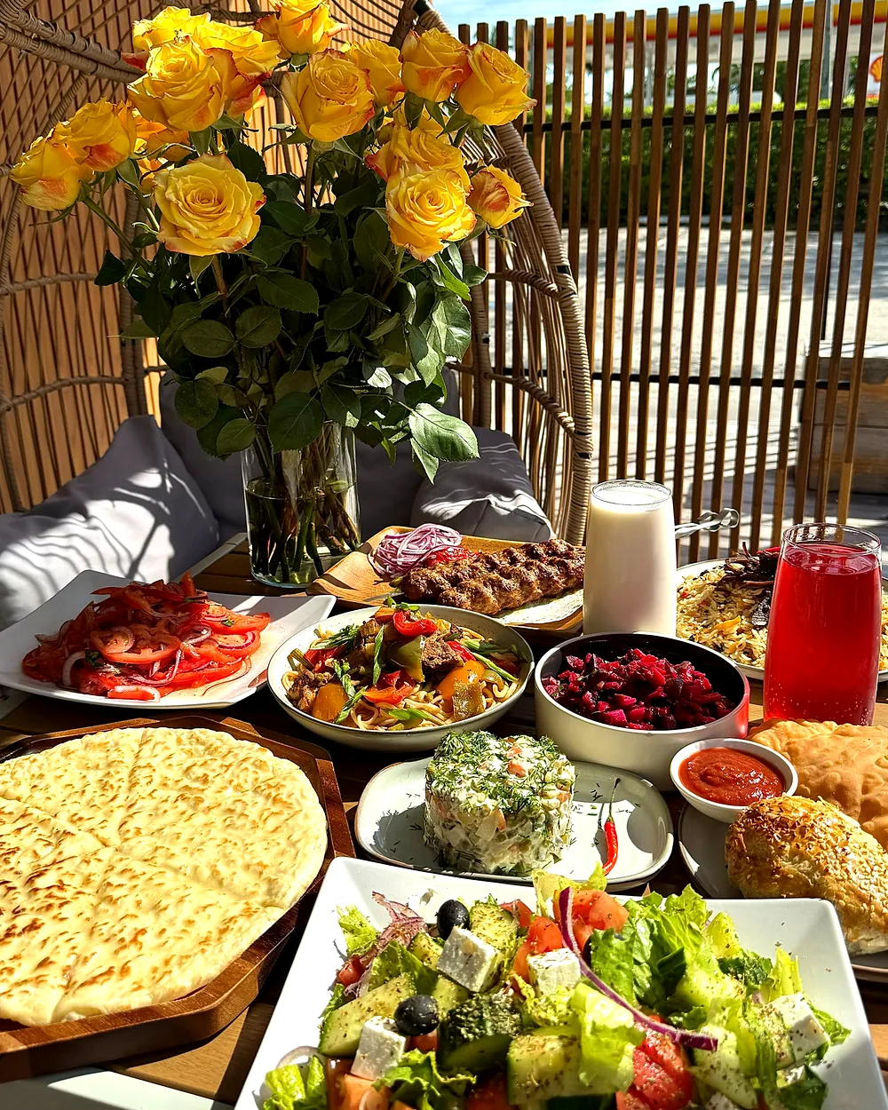 A table at Aurora laid with salads, grilled meat, fresh flatbread and drinks, with yellow roses beside it