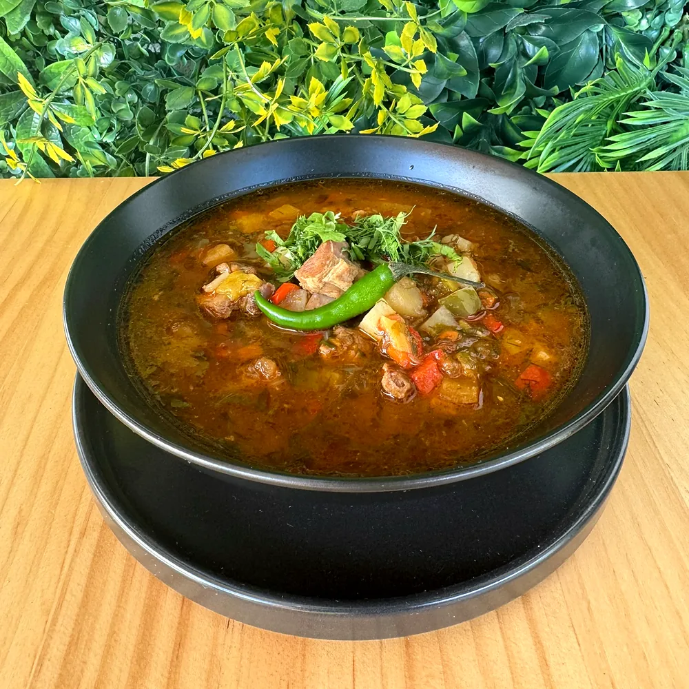 A bowl of soup with beef, vegetables and green chilli